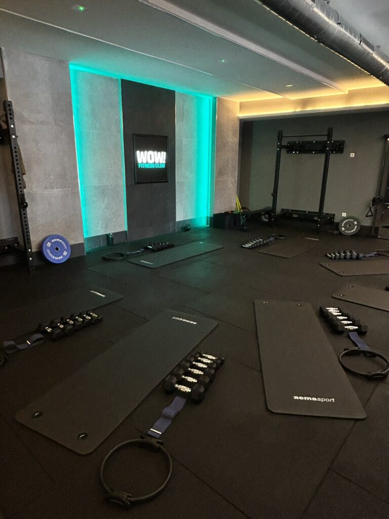 Cartel luminoso de WOW! Fitness Club en la sala de entrenamiento de Colmenar Viejo, con esterillas y mancuernas preparadas